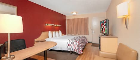 Una habitación de hotel con cama, escritorio, silla y televisor sobre un mueble.