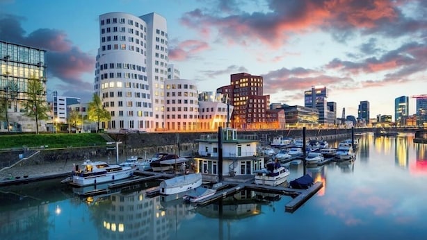 Un puerto deportivo con barcos amarrados, un paseo marítimo y edificios modernos de diseño curvo.
