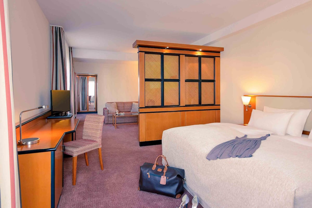 A hotel room with a bed, a desk, a chair, a television, a wardrobe, and a window with a view.