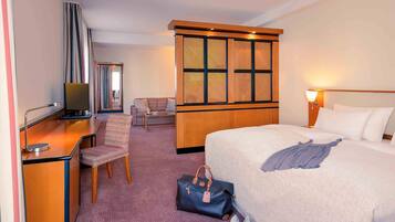 A hotel room with a bed, a desk, a chair, a television, a wardrobe, and a window with a view.