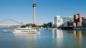 A river with a boat, a tower, and modern buildings. - Mercure Düsseldorf City Center (Düsseldorf)