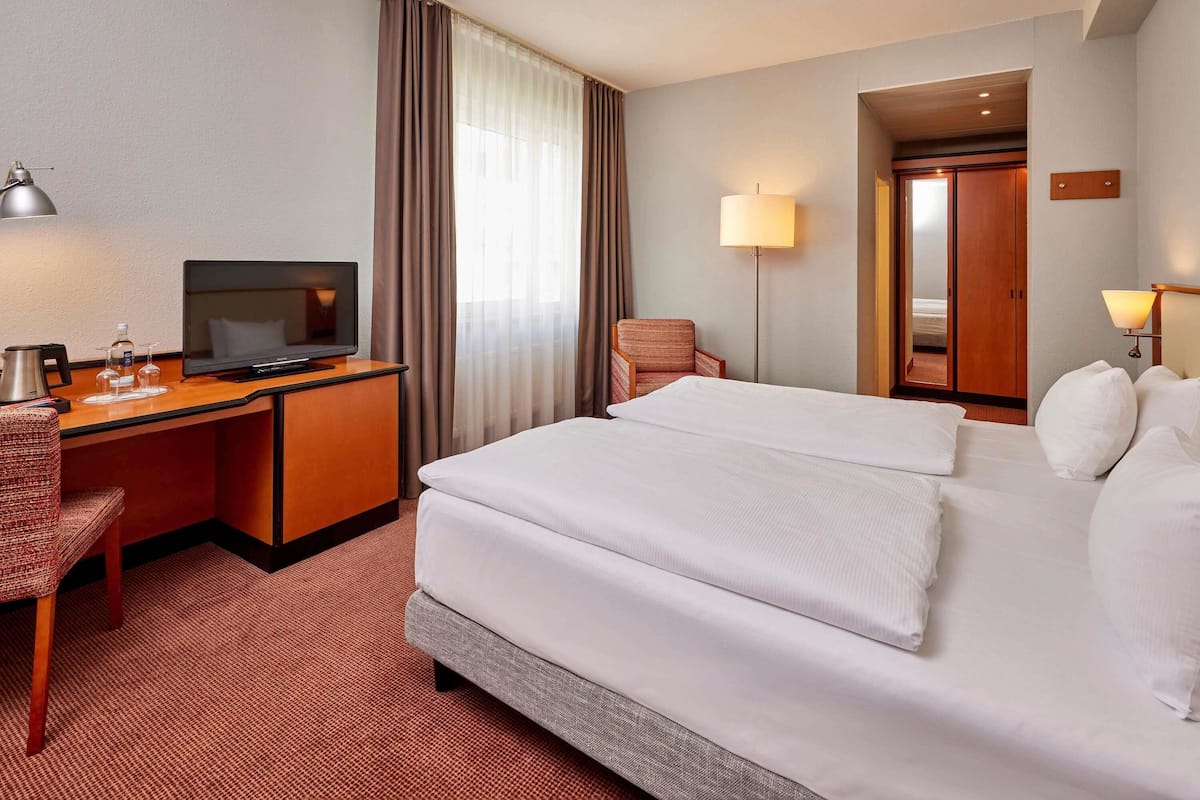 A hotel room with a bed, desk, chair, TV, and a lamp.