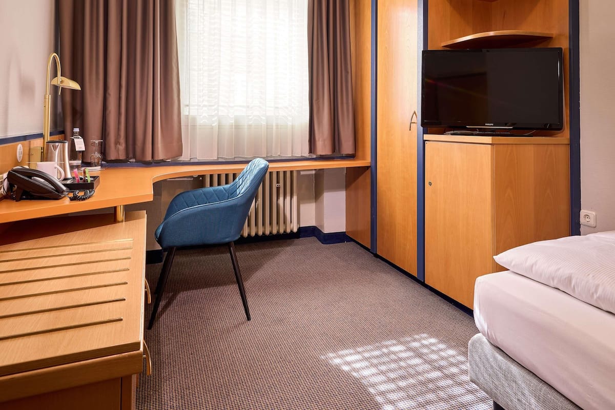 A hotel room with a desk, chair, bed, TV, and a window with curtains.