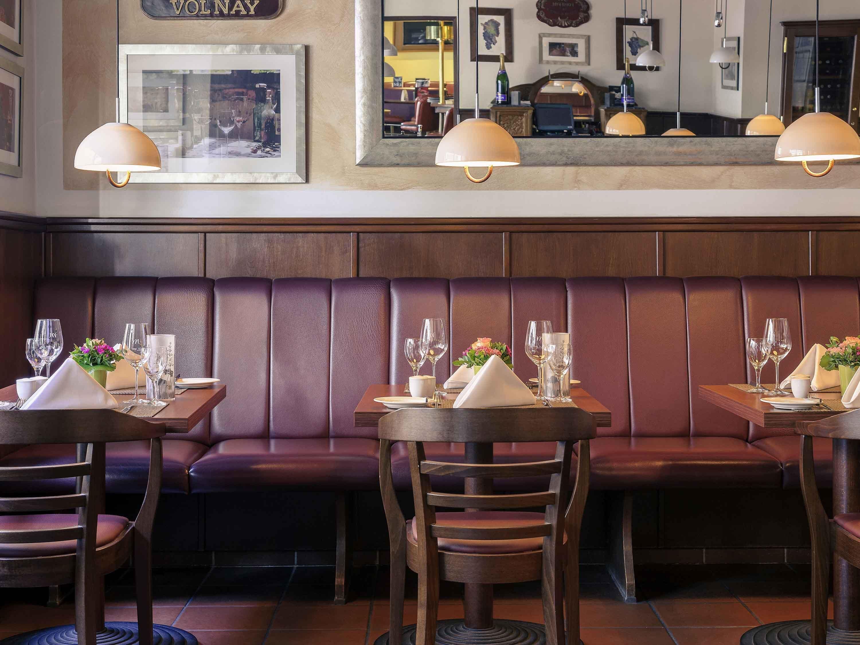 A restaurant with leather booths, wooden tables, and pendant lighting.