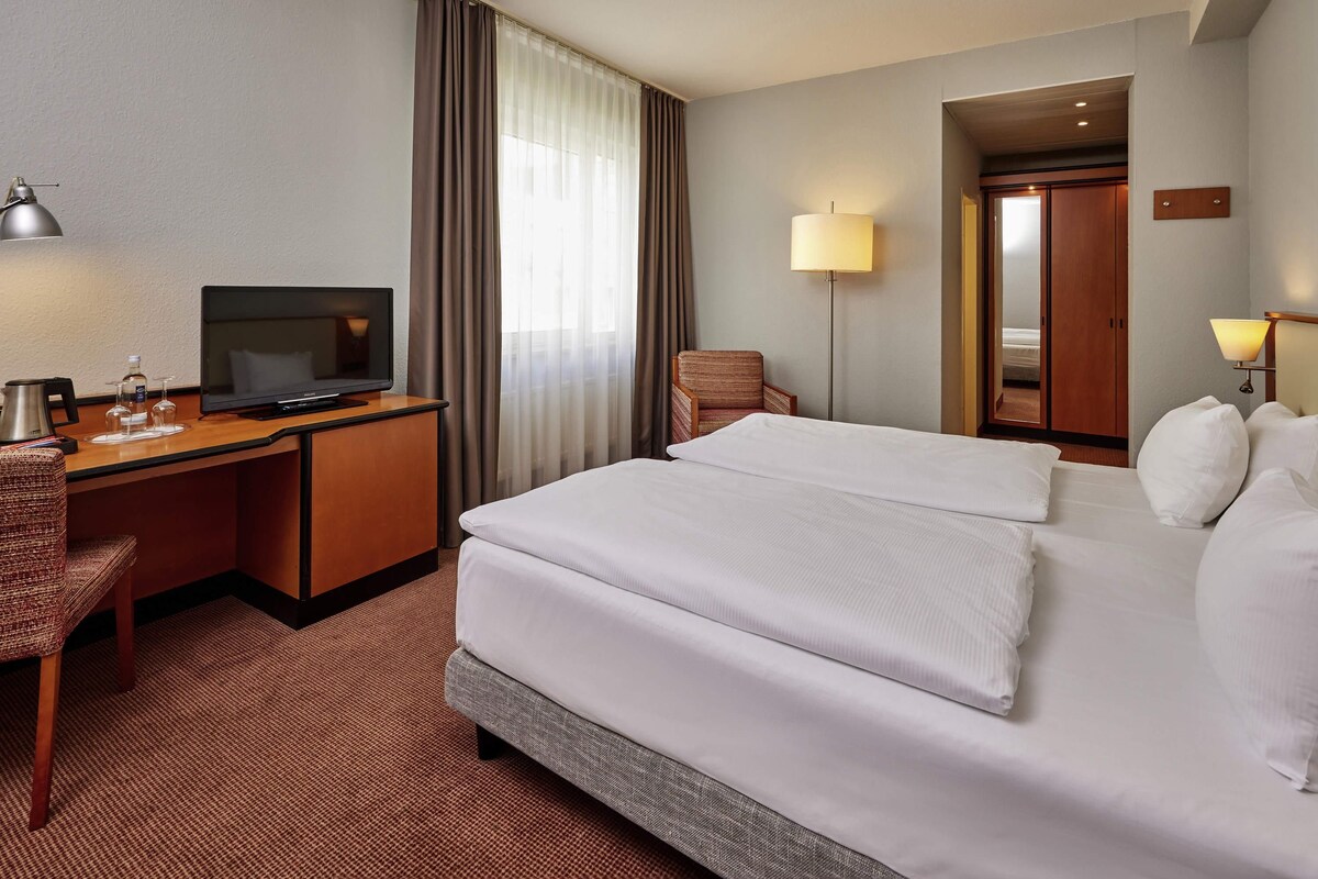Ein Hotelzimmer mit Bett, Schreibtisch, Stuhl, Fernseher und Lampe.