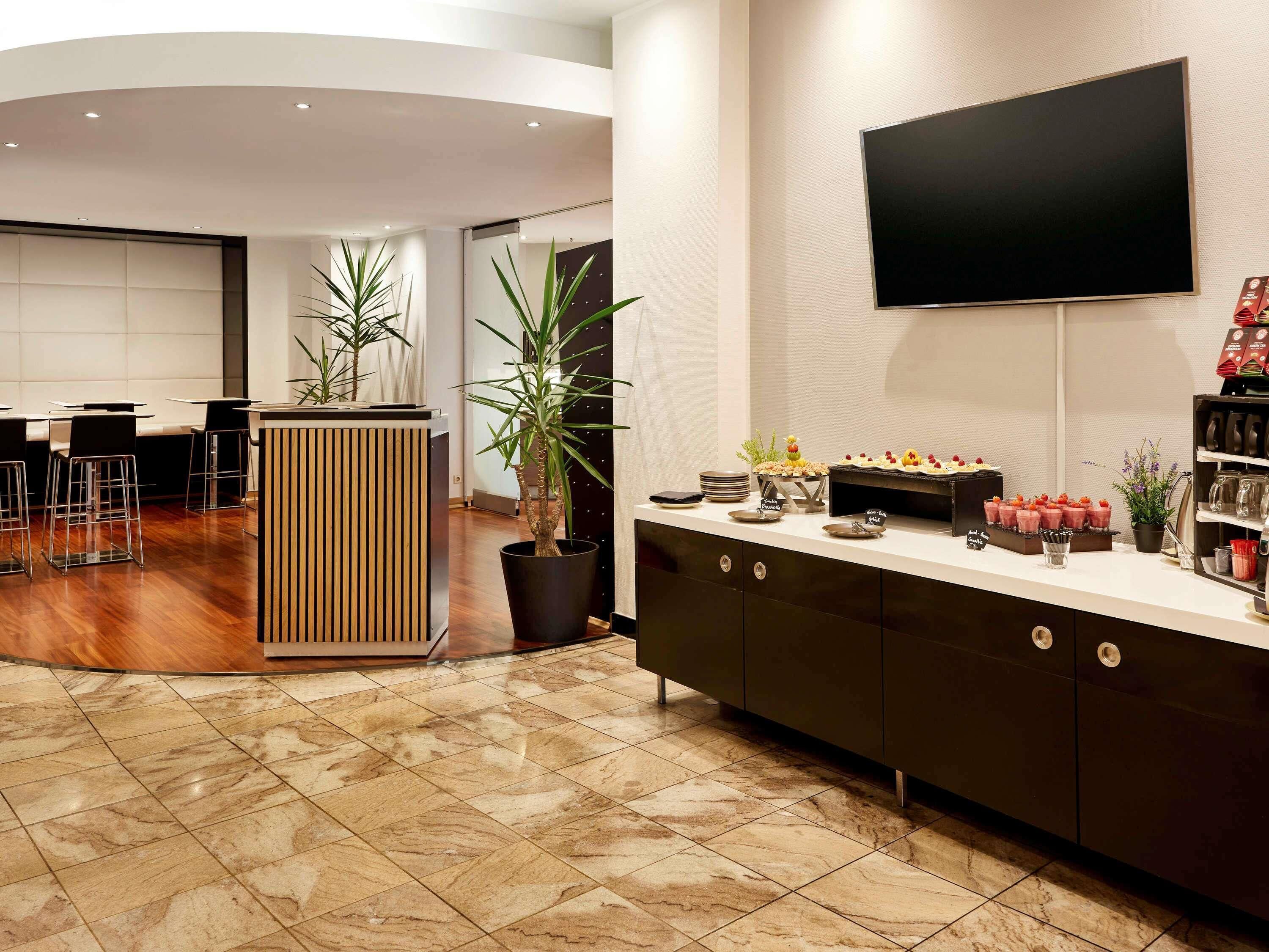 A modern hotel lobby with a reception desk, seating area, and a flat-screen TV mounted on the wall.