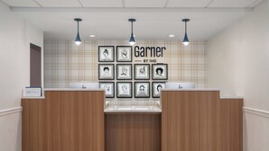 A reception area with wooden reception desks, a check-in counter, and framed artwork on the wall. - Garner Hotel Totowa by IHG (Totowa)