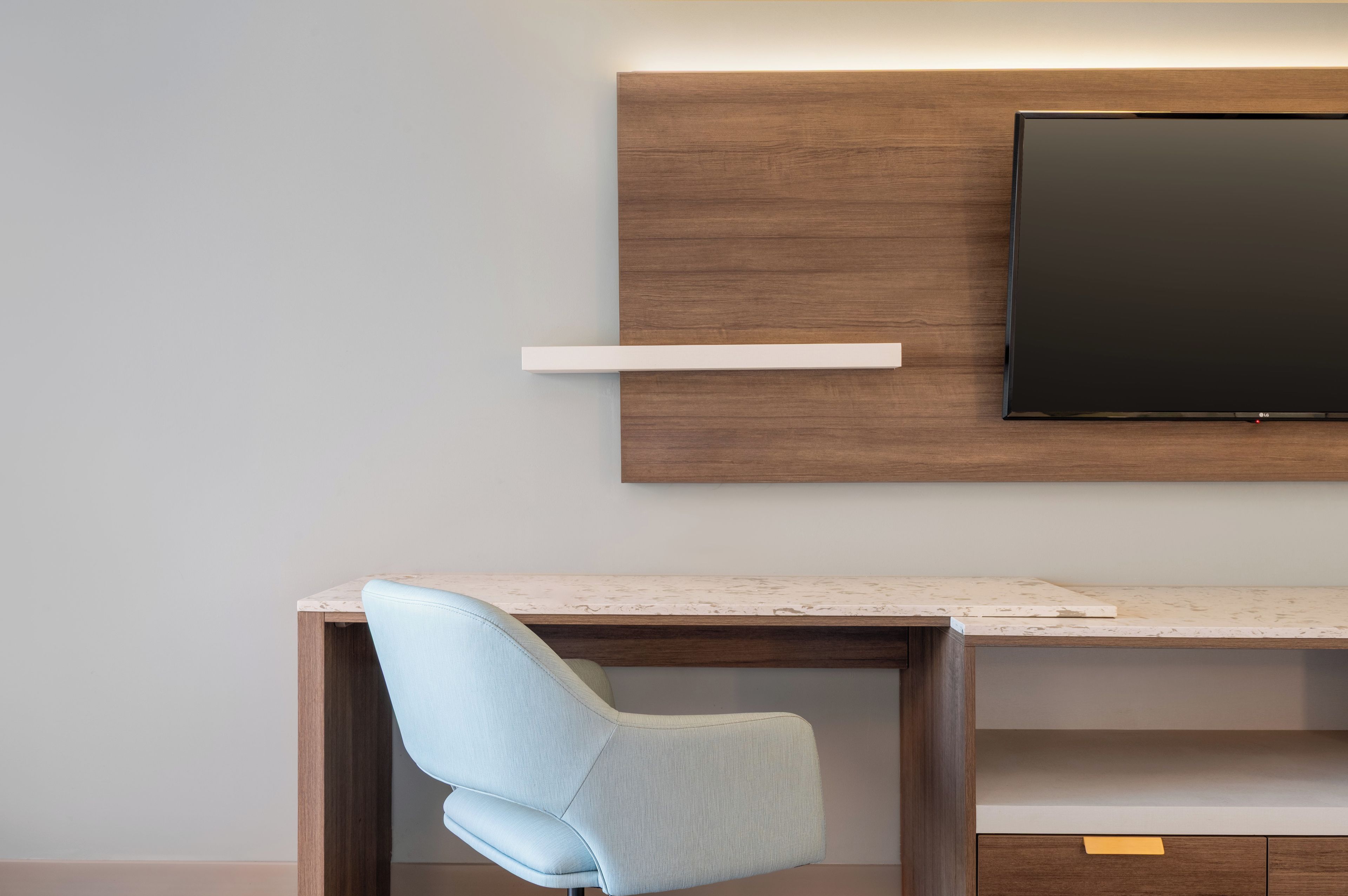 Un espacio de oficina moderno con un escritorio, una silla azul claro, un televisor de pantalla plana montado y una pared de acento de madera.