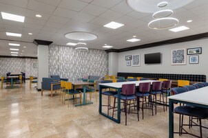 Un comedor moderno con varias mesas y sillas, un televisor de pantalla plana en la pared, y un diseño de papel tapiz estampado.