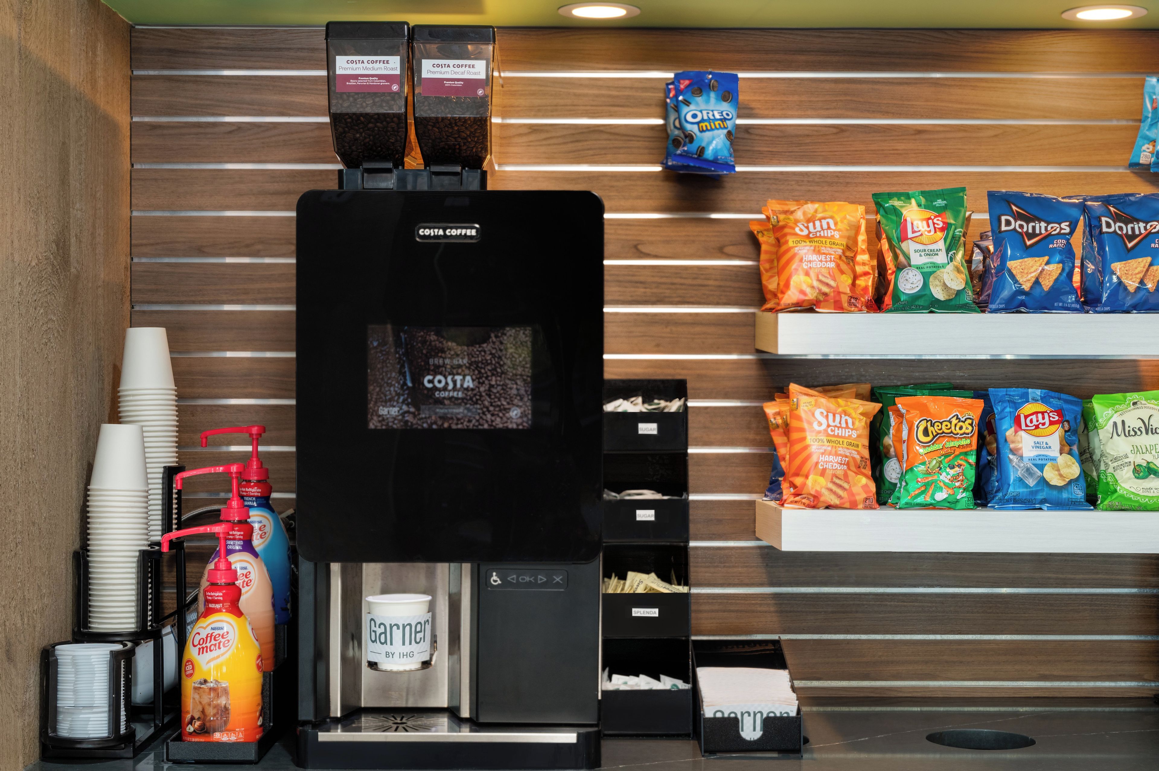 A coffee station with a coffee machine, disposable cups, and a variety of snacks.