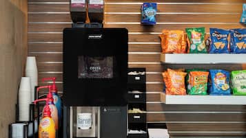 A coffee station with a coffee machine, disposable cups, and a variety of snacks.