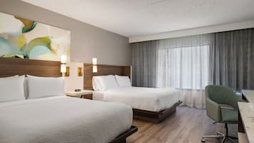 A hotel room with two beds, a desk, a chair, and a large window with curtains.