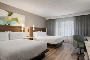 A hotel room with two beds, a desk, a chair, and a large window with curtains.