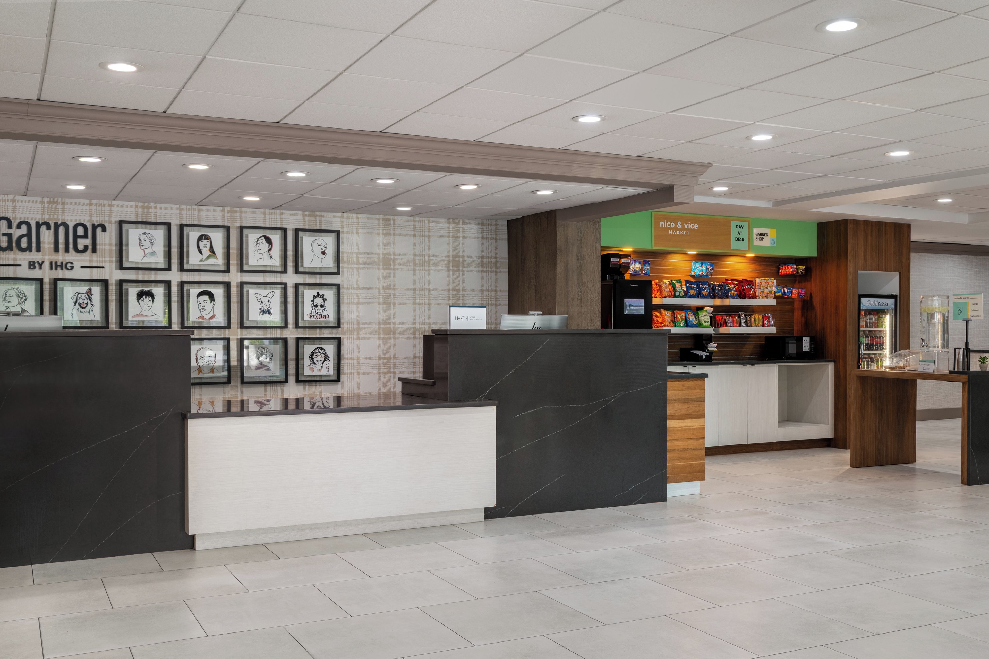 A hotel lobby with a reception desk, framed artwork on the wall, a snack bar, and a 'Pay at Desk' sign.