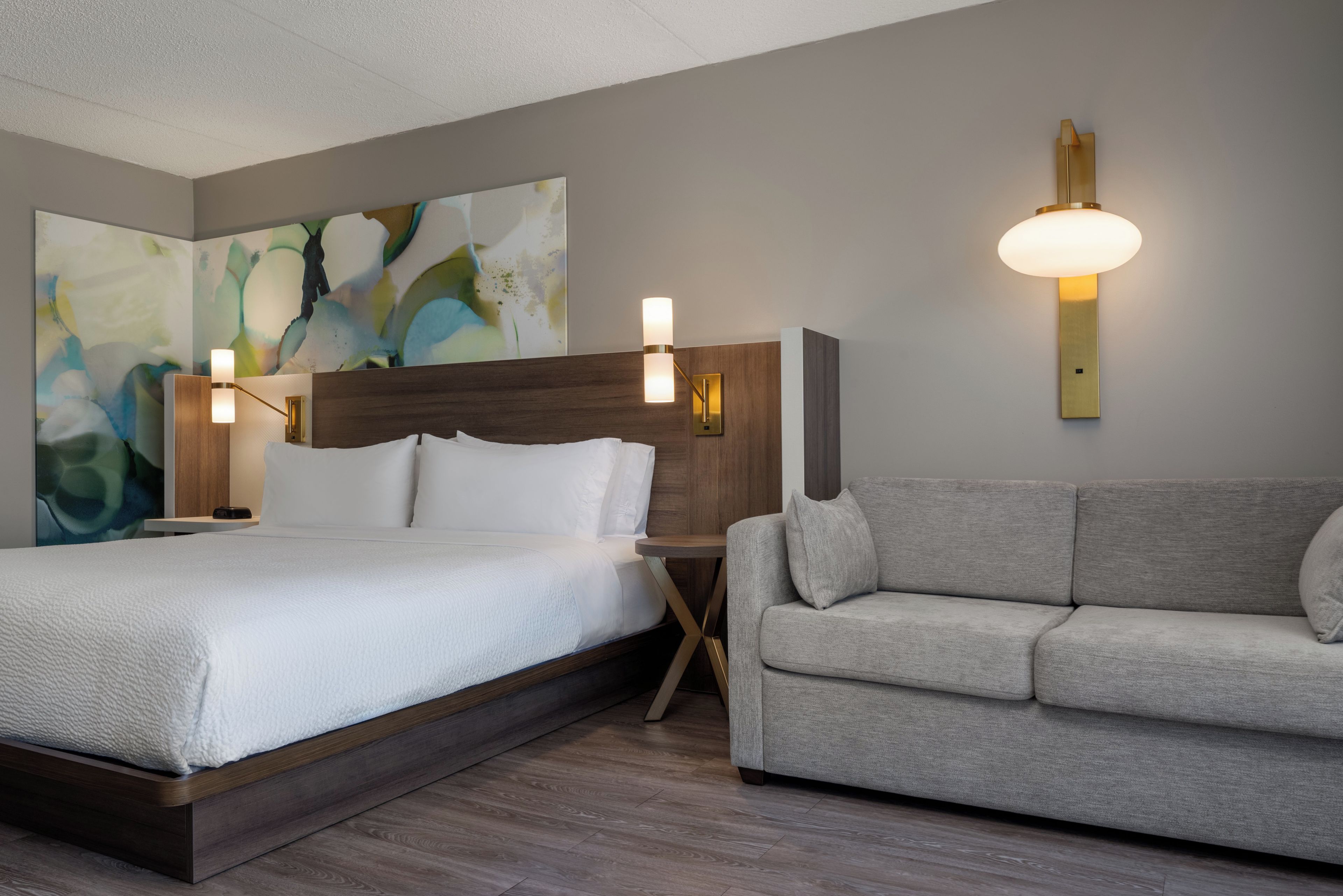 Una habitación de hotel con una cama, un sofá y dos lámparas de pared.