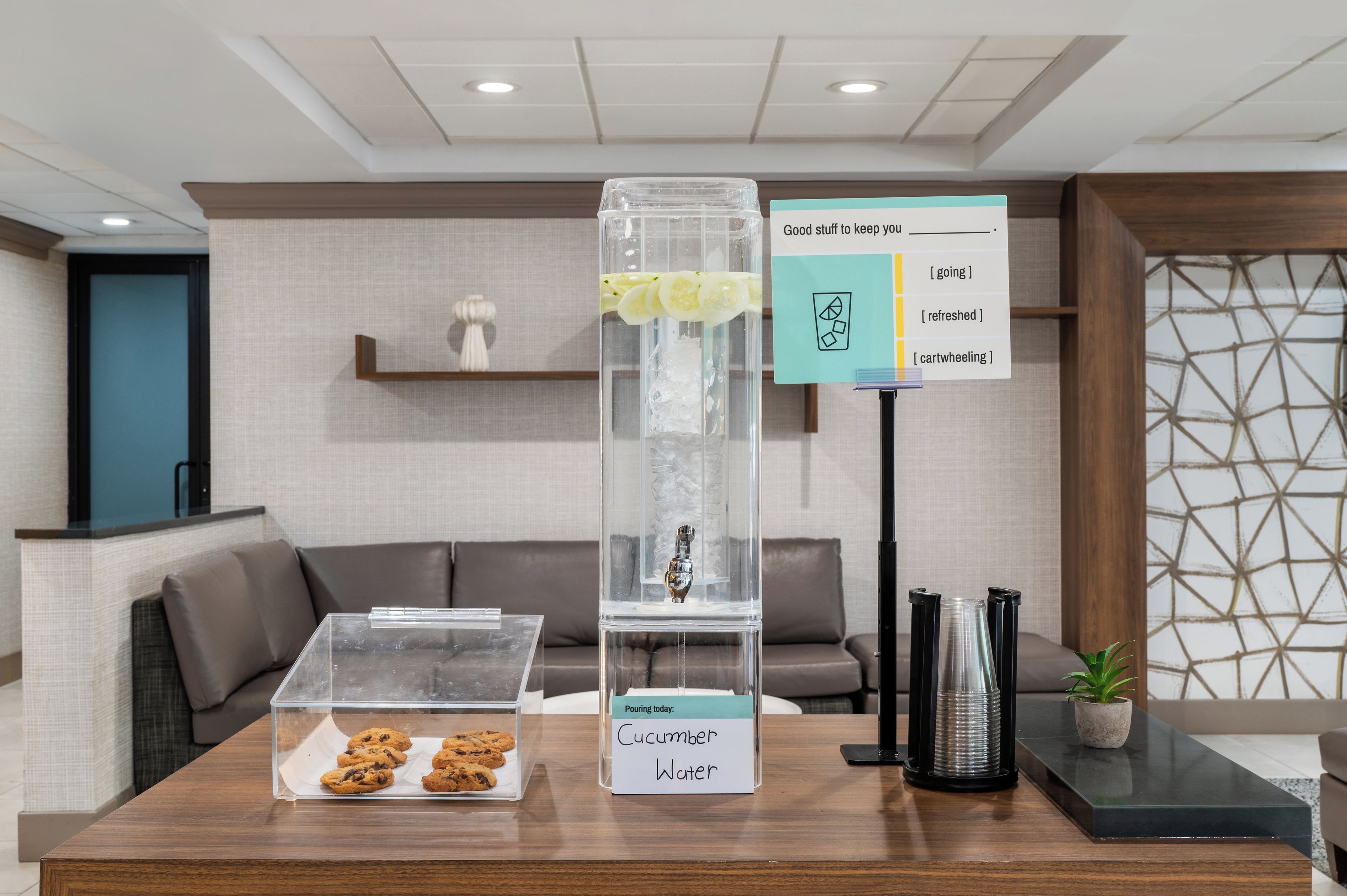 A reception area with a clear display case containing cookies, a water dispenser, and a sign with options for refreshment.