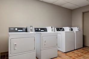 Een wasserette met vier voorladers, wasmachines en drogers, een betegelde vloer en een effen muur.