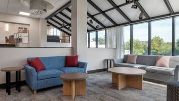 A modern interior with a blue sofa, a grey sofa, two round tables, and a staircase with a railing.