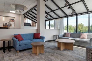 A modern interior with a blue sofa, a grey sofa, two round tables, and a staircase with a railing.