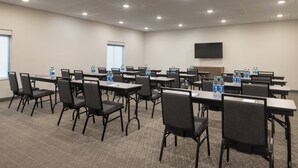 A conference room with multiple tables and chairs, water bottles on each table, and a television mounted on the wall. - Garner Hotel Totowa by IHG (Totowa)