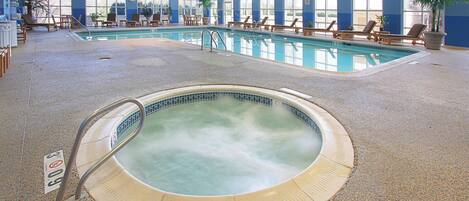 Una piscina interior con un jacuzzi, sillas de descanso y ventanas amplias.