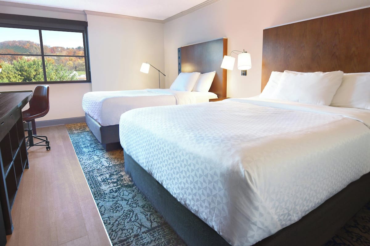 A hotel room with two beds, a desk, and a chair.
