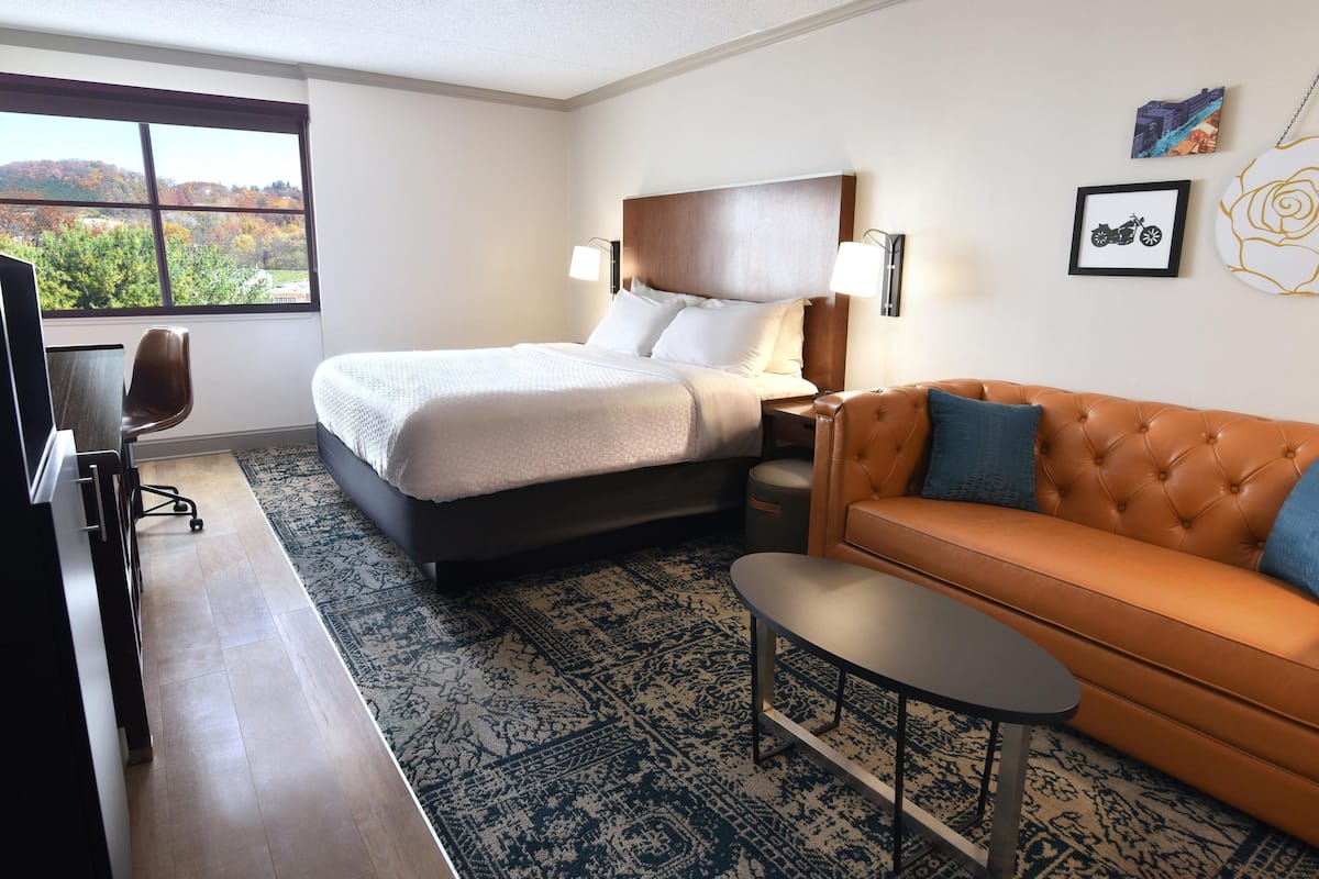 A hotel room with a bed, a sofa, a small table, a desk with a chair, and a TV.