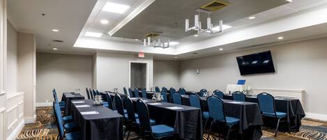 A conference room with tables and chairs, a flat-screen TV on the wall, and a patterned carpet.