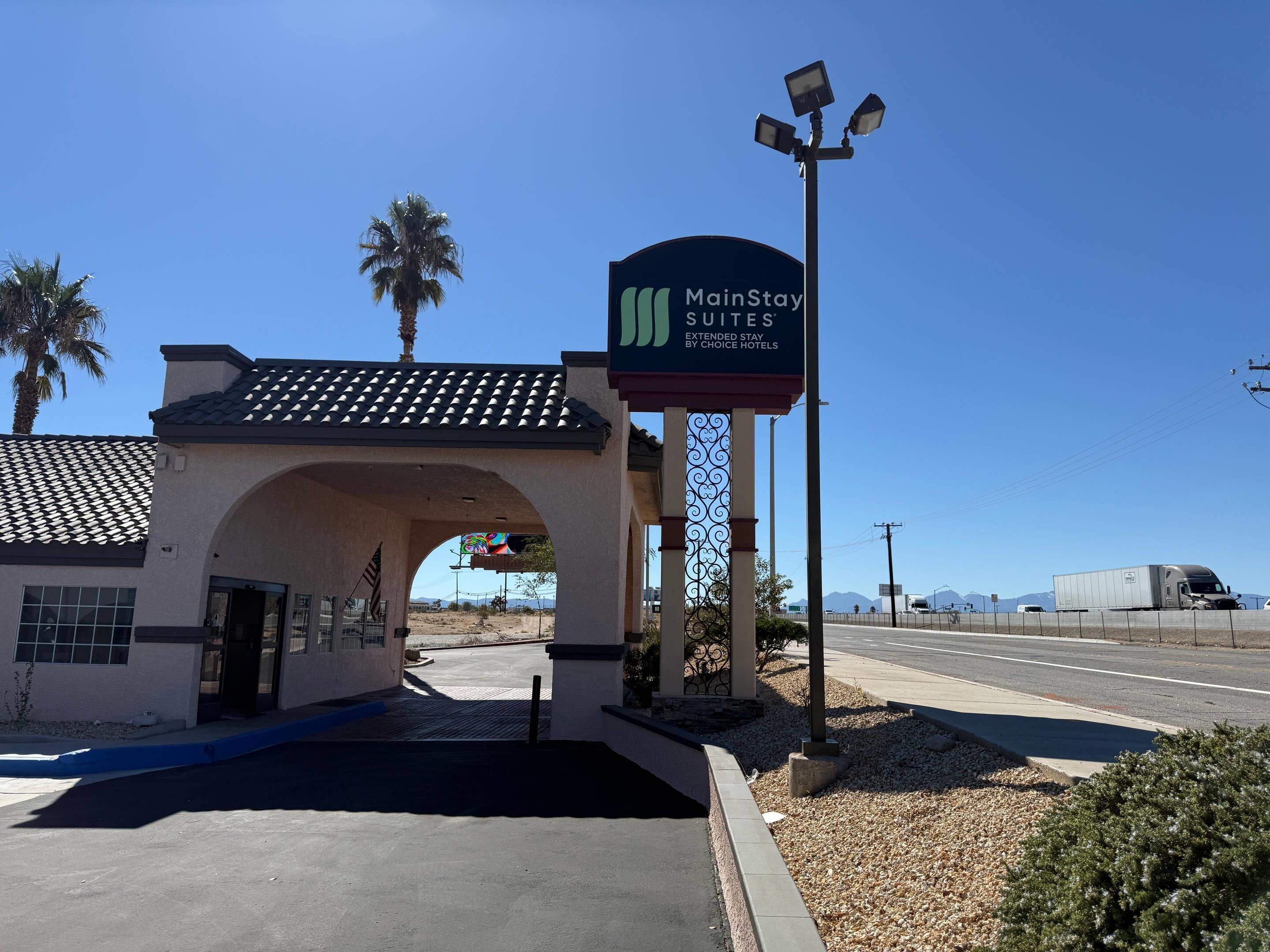 A MainStay Suites sign with a clear sky and palm trees in the background.
