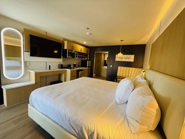 Ett modernt hotellrum med en stor säng, ett inbyggt skrivbord, en platt-TV och ett litet pentry.