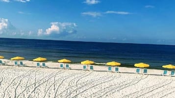 A beach with rows of yellow umbrellas and green chairs facing the ocean.