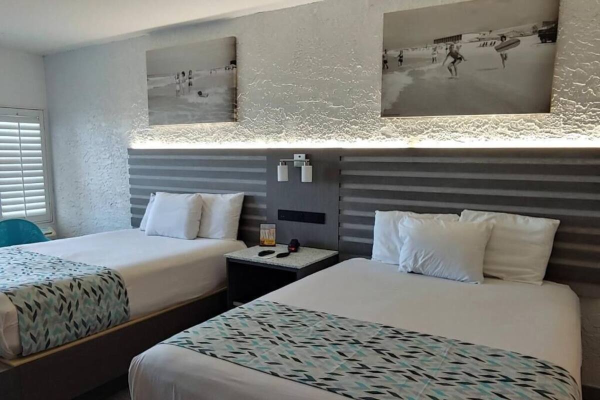 A hotel room with two beds, a nightstand, and a wall-mounted light fixture.