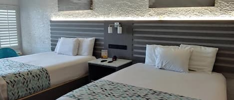 A hotel room with two beds, a nightstand, and a wall-mounted light fixture.