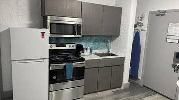 A compact kitchen with a refrigerator, stove, microwave, and sink.