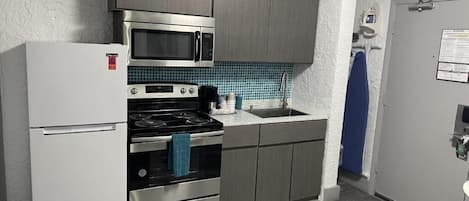 A compact kitchen with a refrigerator, stove, microwave, and sink.