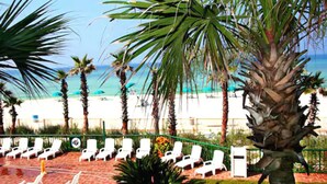 A beachside lounge with white lounge chairs and a palm tree. - Casa Loma Inn (Panama City Beach)