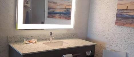 A bathroom with a large mirror, a sink, a towel rack, and a chair.