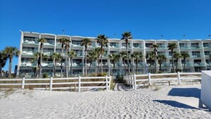 A beachfront hotel with multiple balconies, palm trees, and a white fence. - Casa Loma Inn (Panama City Beach)