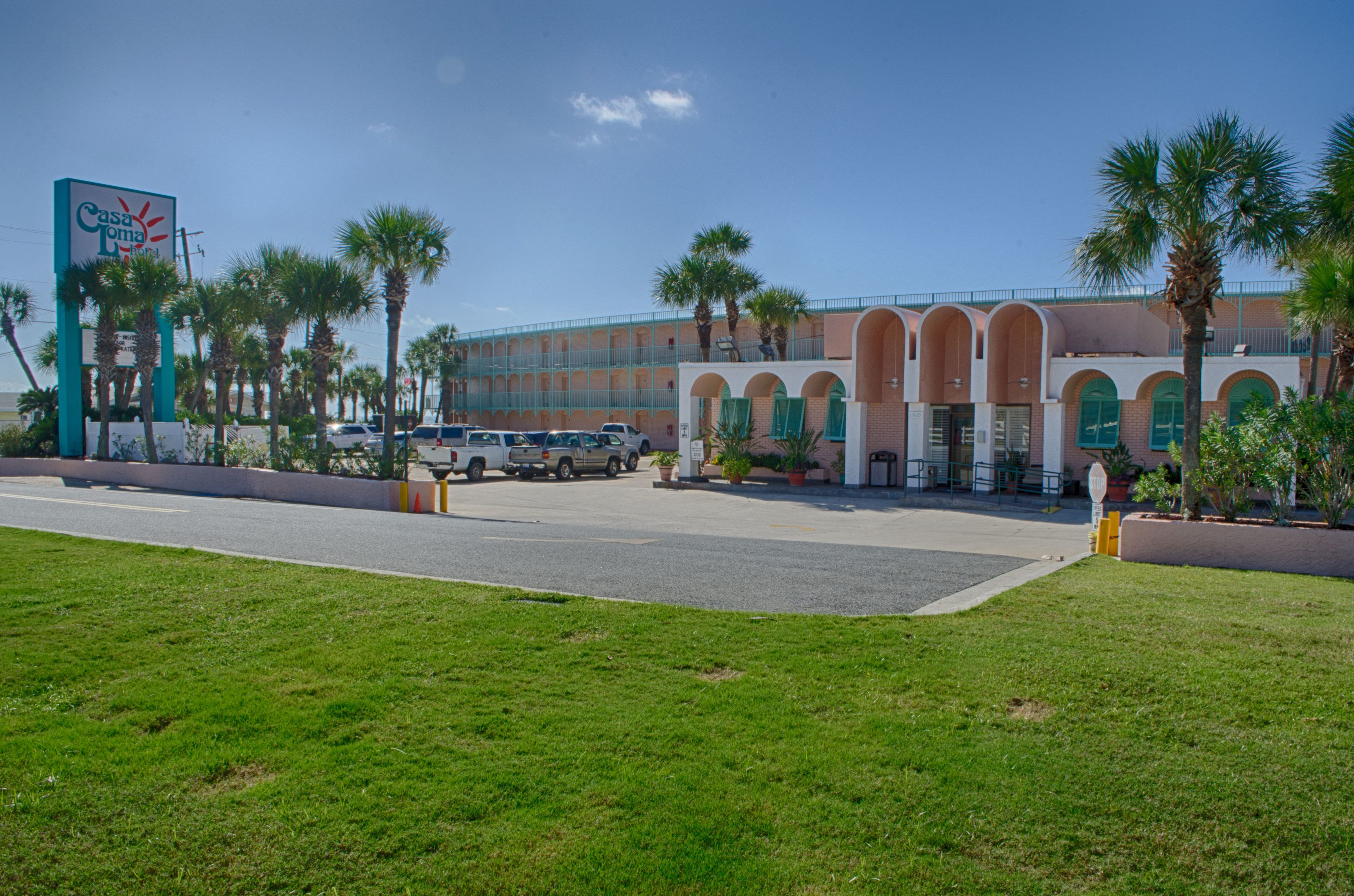 A hotel with a large sign, multiple parking spaces, and palm trees.