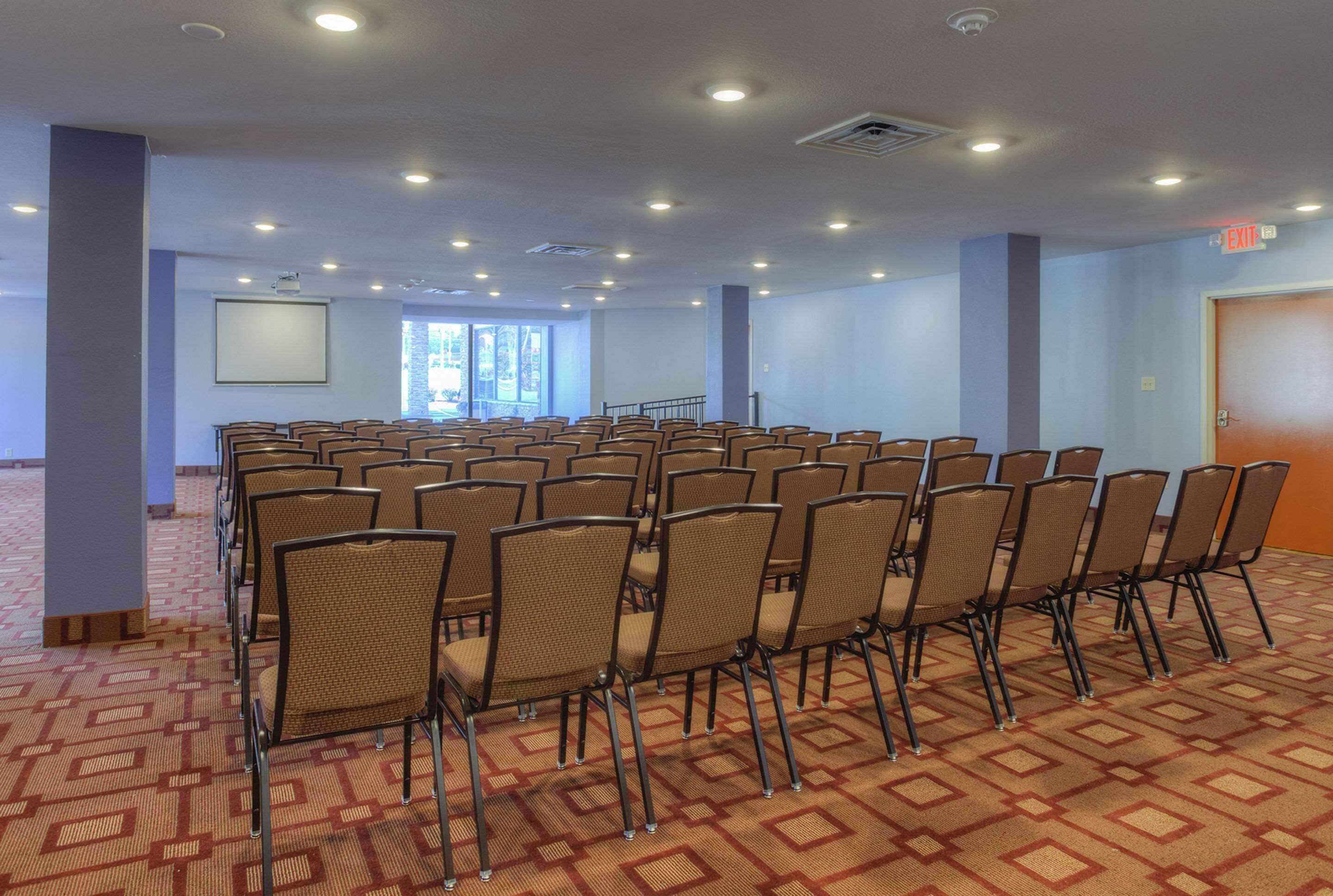 A conference room with rows of chairs, a projector screen, and a carpeted floor.