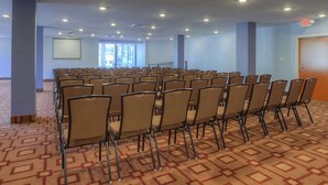Une salle de conférence avec des rangées de chaises, un écran de projection et un sol recouvert de moquette.