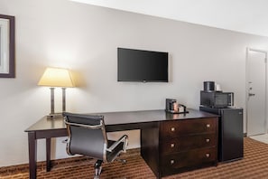 A hotel room with a desk, chair, flat-screen TV, lamp, coffee maker, microwave, refrigerator, and a door. - Quality Inn & Suites Chattanooga-East Ridge (Chattanooga)