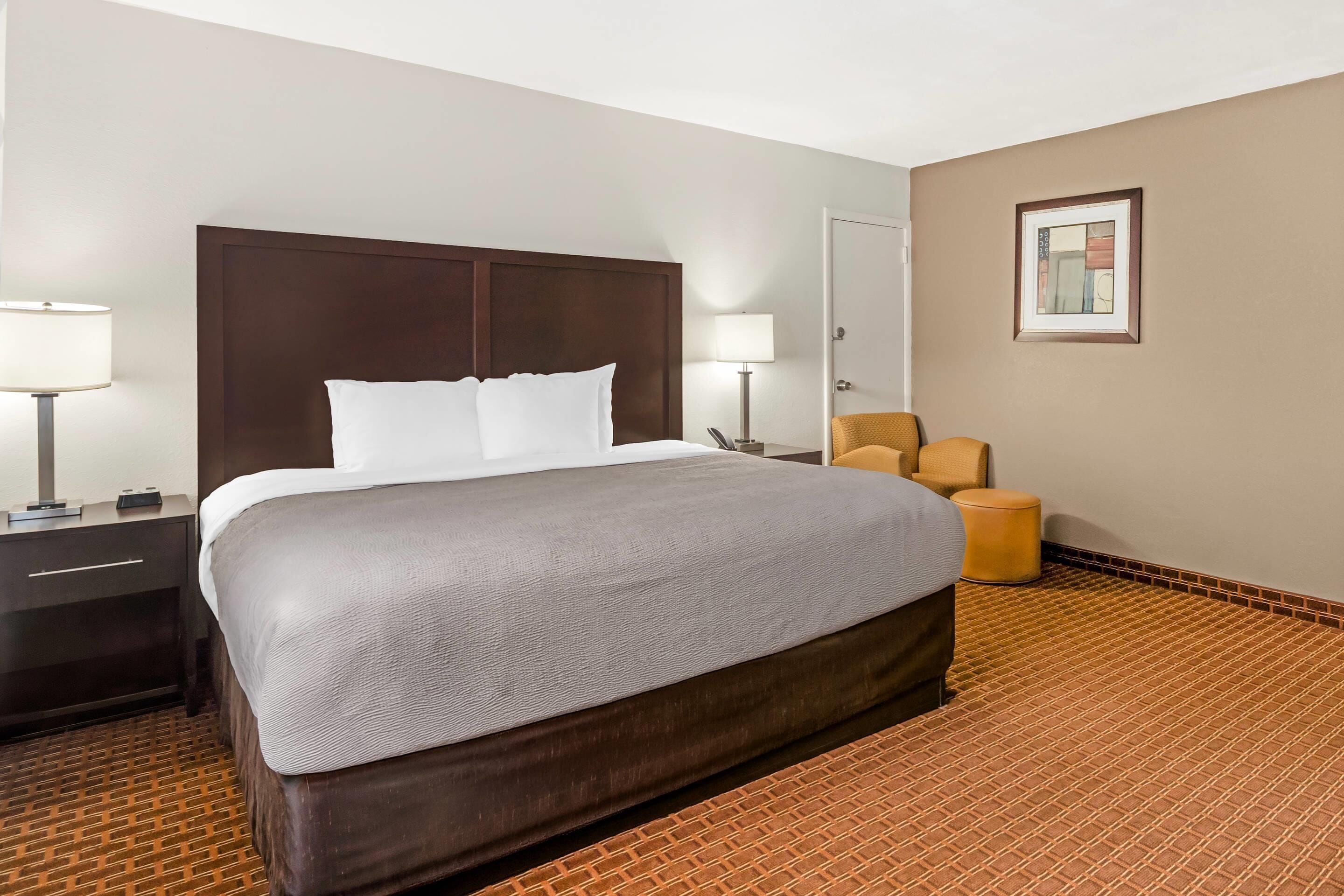 A hotel room with a large bed, two bedside tables, a chair, and a door.