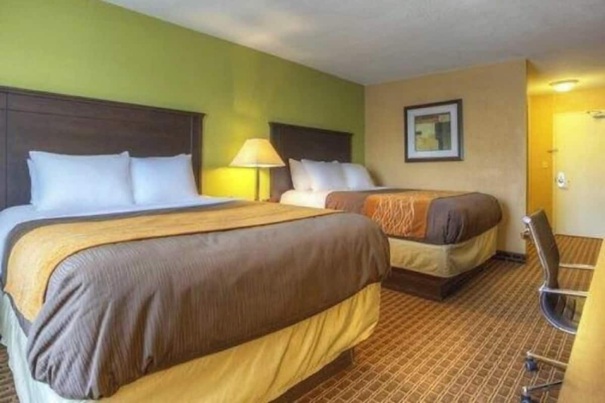 Una habitación de hotel con dos camas, un escritorio, una silla y una lámpara.