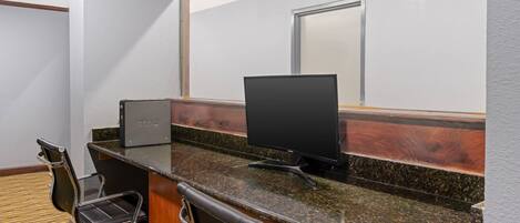 Quarto de hotel com uma mesa, duas cadeiras, um computador e uma janela grande.