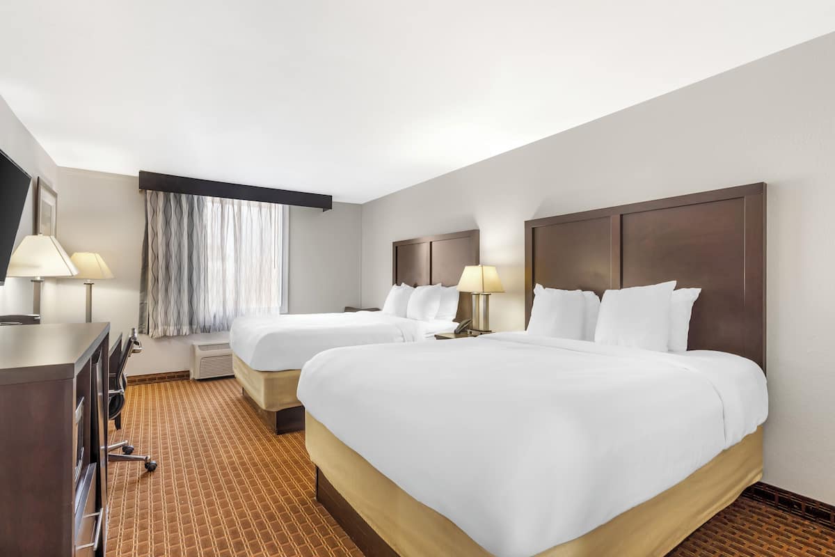 Habitación de hotel con dos camas, un escritorio y una ventana con cortinas.