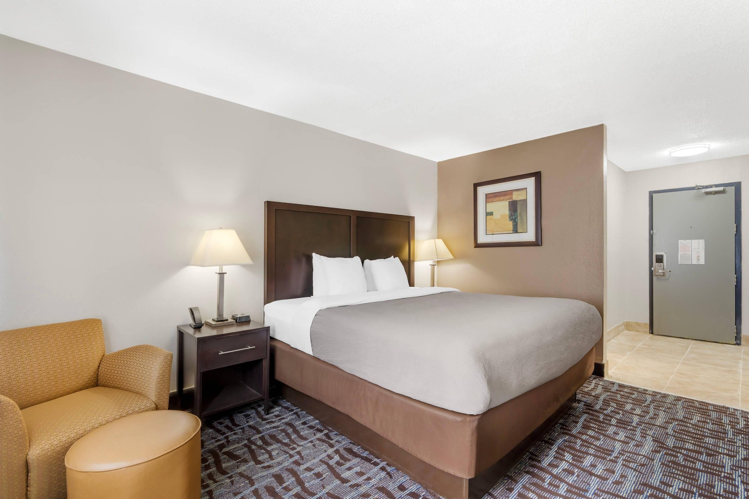A hotel room with a bed, two bedside lamps, a nightstand, a chair, and a door.