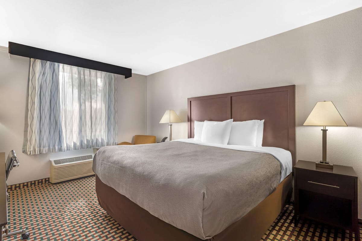 Habitación de hotel con una cama grande, dos lámparas de noche, una silla, un escritorio y una ventana con cortinas.