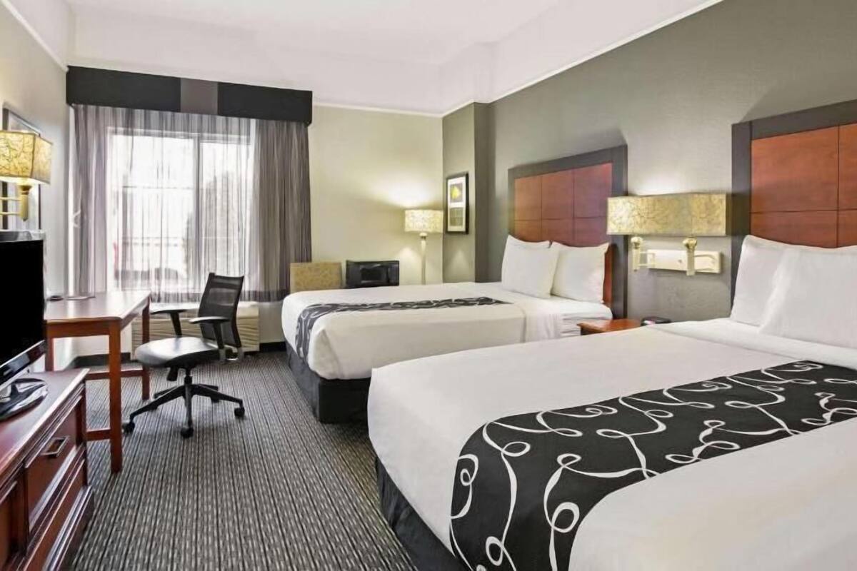 Une chambre d’hôtel avec deux lits, un bureau avec une télévision et une chaise.