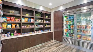 Zona de aperitivos y bebidas con estantes llenos de papas fritas, bocadillos y una sección refrigerada con bebidas.